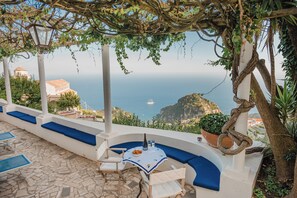 A terrace with a table and chairs, overlooking a coastal view with a boat in the distance. - Villa Campanella by Elite Villas (Ravello)