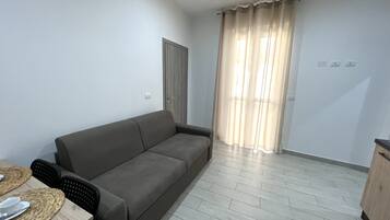 A modern living room with a grey sofa, a dining table with chairs, and a wooden cabinet.