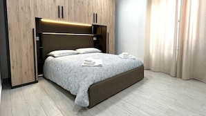 Une chambre à coucher moderne avec une tête de lit en bois, un lit recouvert d’une couvre-lit à motifs et un plancher en bois de couleur claire.