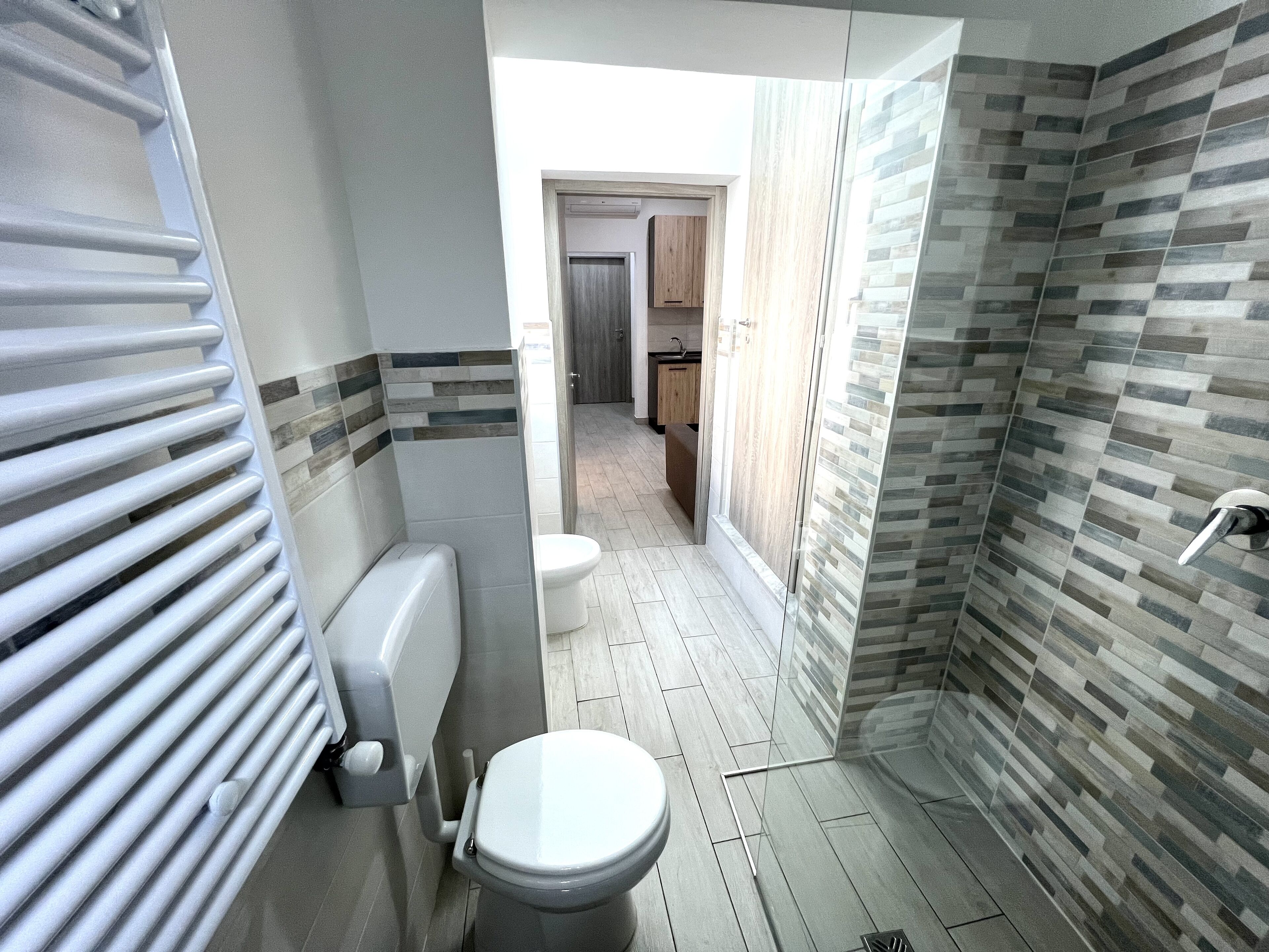 Un bagno moderno con doccia, WC e vista sulla cucina.