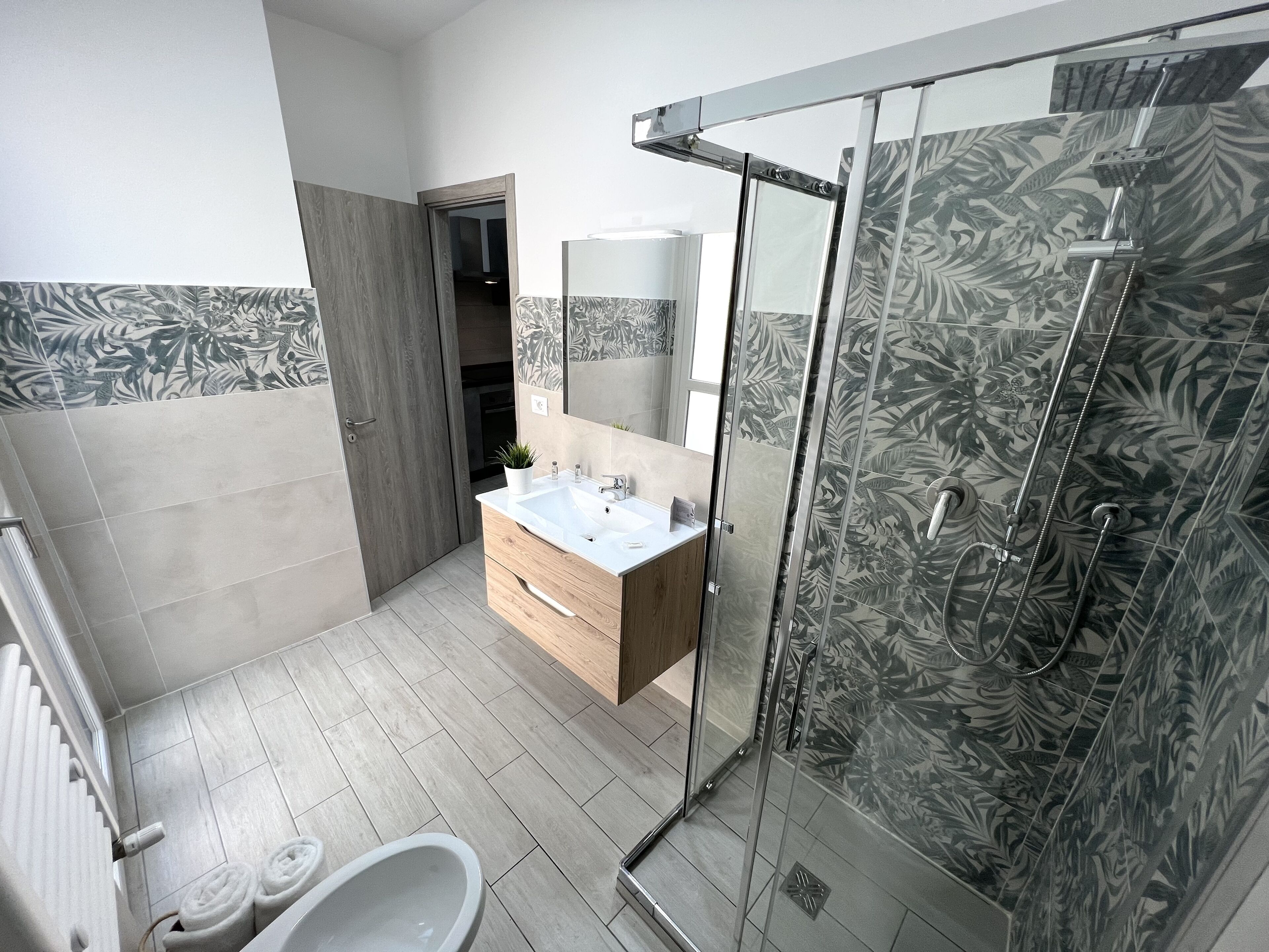 Un bagno moderno con cabina doccia in vetro, un mobile bagno in legno e un lavandino bianco.