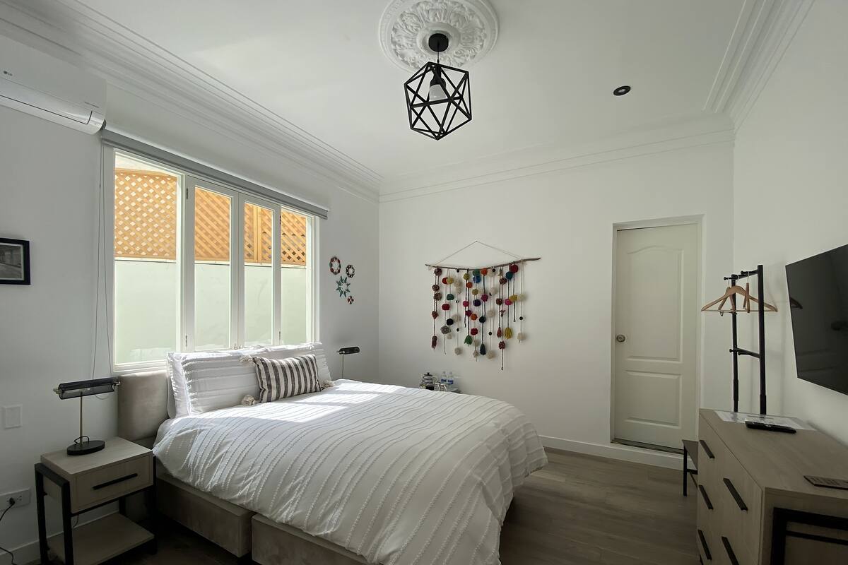 Een slaapkamer met een bed, nachtkastjes, een hanglamp, een kledingkast en een tv op een standaard.