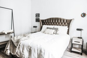 A neatly arranged bedroom with a tufted headboard bed, a bedside table with a lamp, and a wall-mounted shelf with a mirror. - WasiPai Boutique Hotel (Lima)