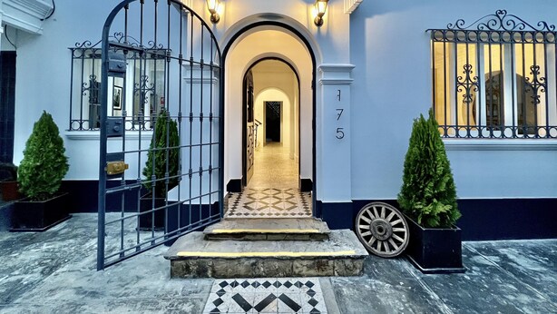 A grand entrance with a gated driveway, a tiled pathway leading to an archway, and a number '175' on the wall.
