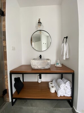 A bathroom with a round mirror, a wooden vanity, a towel rack, and a shelf with towels and toiletries. - WasiPai Boutique Hotel (Lima)
