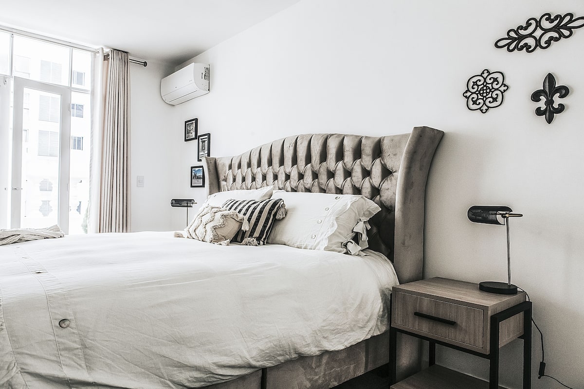Een netjes opgemaakt bed met hoofdeinde, een nachtkastje met lamp en decoratieve wandkunst.