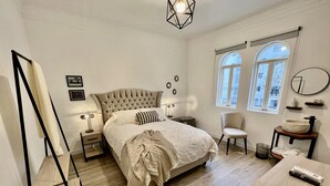A bedroom with a large bed, bedside tables, a chair, a desk, and a window with a view.