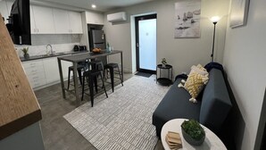 A modern apartment with a kitchen, dining area, and living room. It includes a sofa, a small table with a plant, and a dining table with chairs. - Devonport Loft Apartment: A/C Great Location! (Devonport)