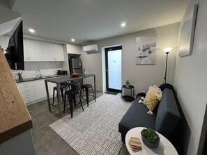 Eine moderne Wohnung mit Küche, Essbereich und Wohnzimmer. Sie umfasst ein Sofa, einen kleinen Tisch mit einer Pflanze und einen Esstisch mit Stühlen.