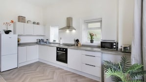 A modern kitchen with white cabinetry, a built-in oven, a microwave, and a window with blinds.