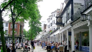 Una concurrida calle peatonal bordeada de tiendas y cafés, con pavimento de piedra, árboles y arquitectura tradicional.