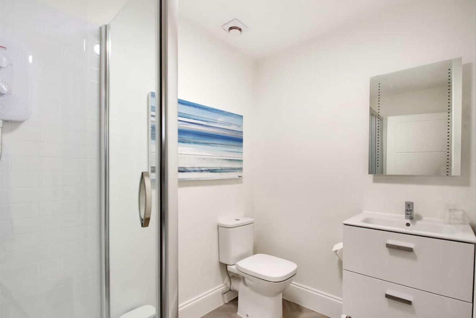 Ein modernes Badezimmer mit Duschkabine aus Glas, Toilette, Waschbecken mit Spiegel und einem Bild an der Wand.