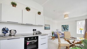A modern kitchen with white cabinets, a built-in oven, and a dining area with a glass table and wicker chairs. - Stunning 2-bed Apartment in Tunbridge Wells (Royal Tunbridge Wells)