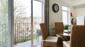 A dining area with wicker chairs and a glass table, a clock on the wall, and a view of the outdoors through large windows. - Stunning 2-bed Apartment in Tunbridge Wells (Royal Tunbridge Wells)