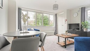 Un salon moderne avec une table à manger ronde, des chaises grises, un canapé bleu et un téléviseur posé sur un meuble noir.