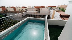 Una piscina en la azotea con barandilla blanca, rodeada de edificios.
