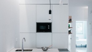 Una cocina moderna con armarios blancos, microondas integrado y una isla central con un cuenco de fruta y vasos.