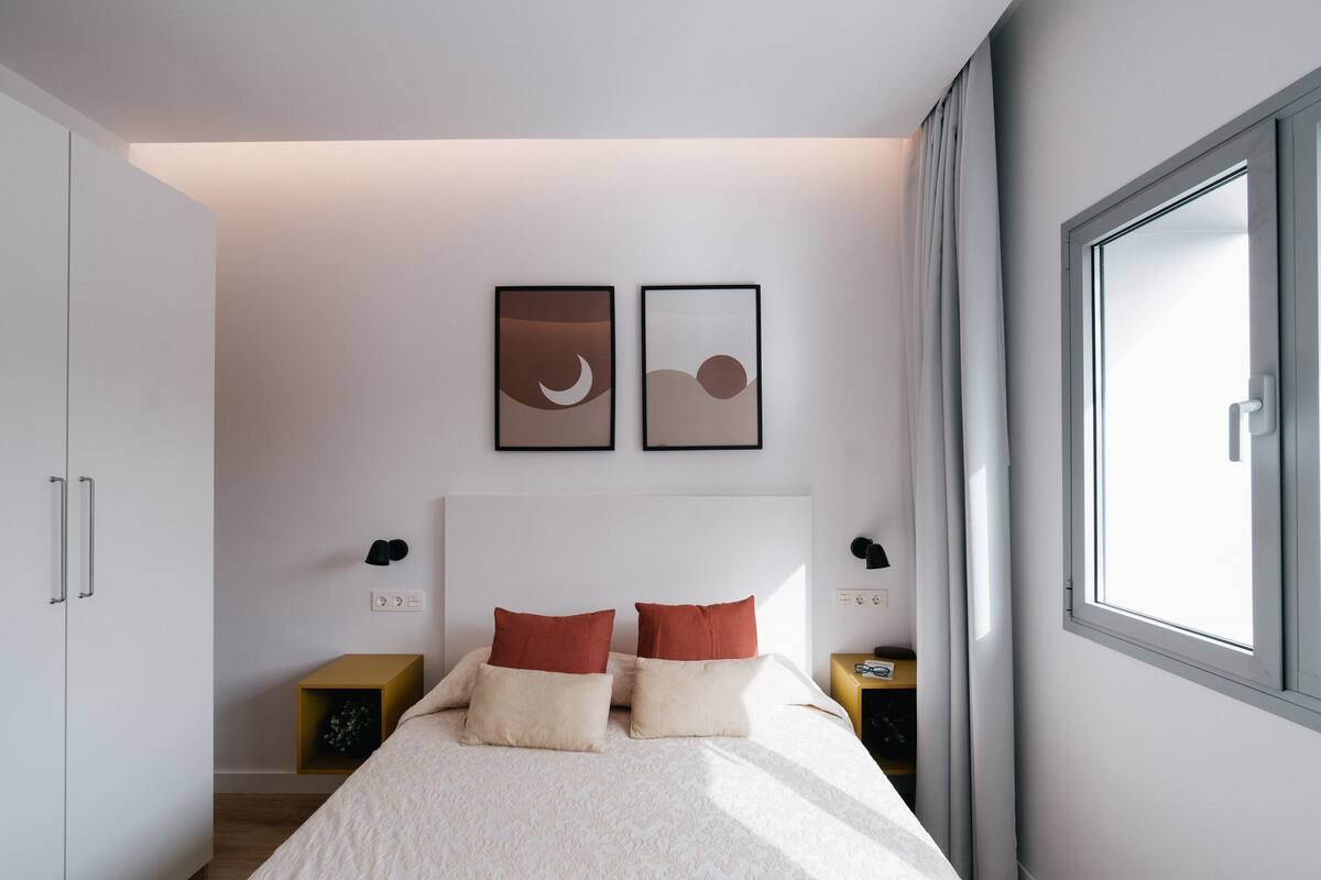 A bedroom with a bed, two bedside tables, a wardrobe, and two framed pictures on the wall.