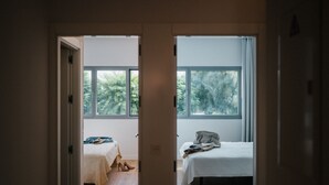 Un dormitorio con dos camas, una ventana y una puerta que da a otra habitación.