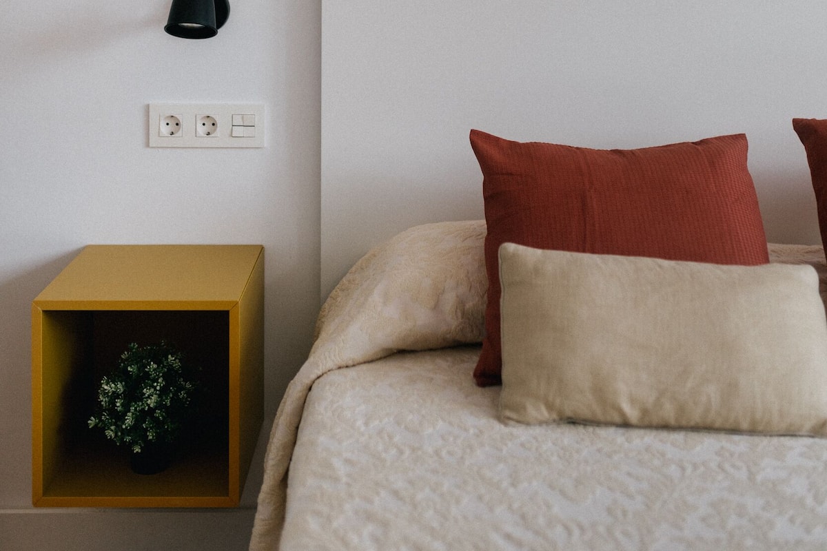 A bedroom with a bed, a nightstand, a wall-mounted lamp, and framed artwork.