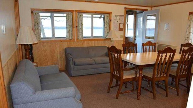 A room with a sofa, a dining table with chairs, and a window with curtains. - Family vacation on Black Lake with a private beach! (Hammond)