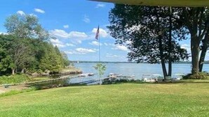 A grassy area with a flagpole, a body of water, and boats in the background. - Family vacation on Black Lake with a private beach! (Hammond)