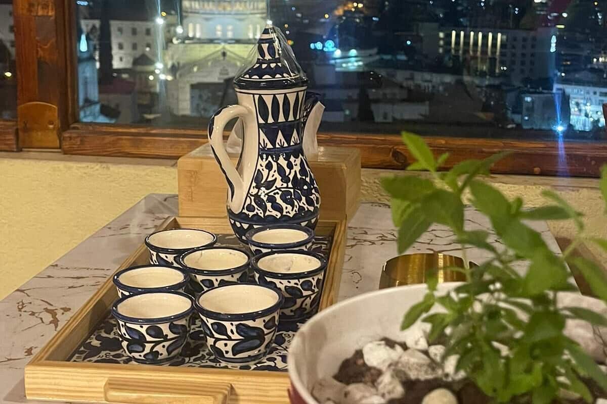 A cityscape view through a window, a decorative pitcher, a tray with cups, and a potted plant on a table.