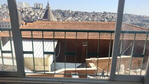 A view from a balcony with a metal railing, overlooking a cityscape with buildings and a prominent dome structure. - Seedi Yousef Hostel & cafe (Nazareth)