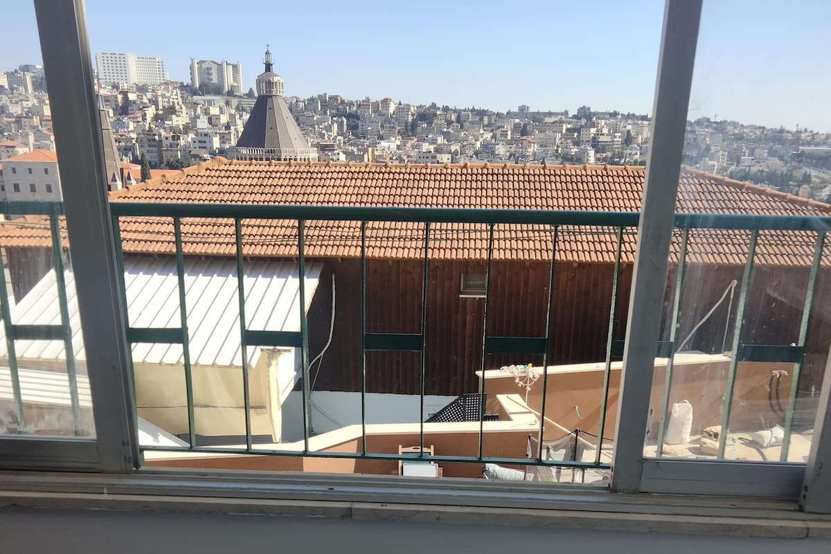 A view from a balcony with a metal railing, overlooking a cityscape with buildings and a prominent dome structure.