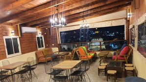 A cozy interior with wooden beams, a dining area with metal chairs, and a seating area with colorful cushions. - Seedi Yousef Hostel & cafe (Nazareth)