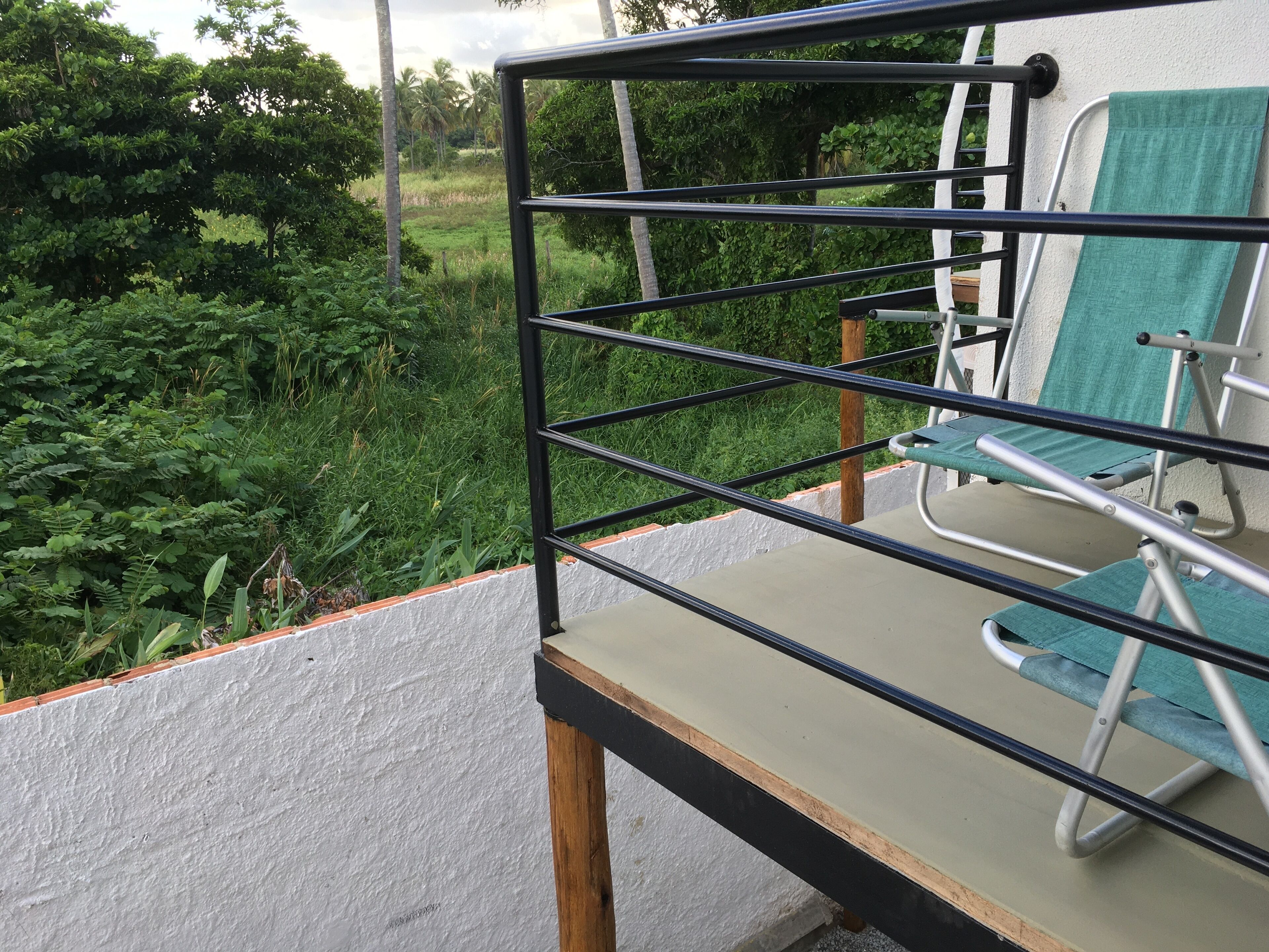 Un balcón con baranda de metal, una silla verde y vistas a un jardín exuberante.