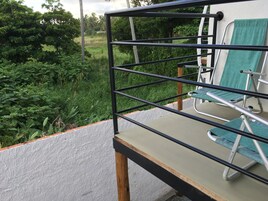 Un balcón con baranda de metal, una silla verde y vistas a un jardín exuberante.