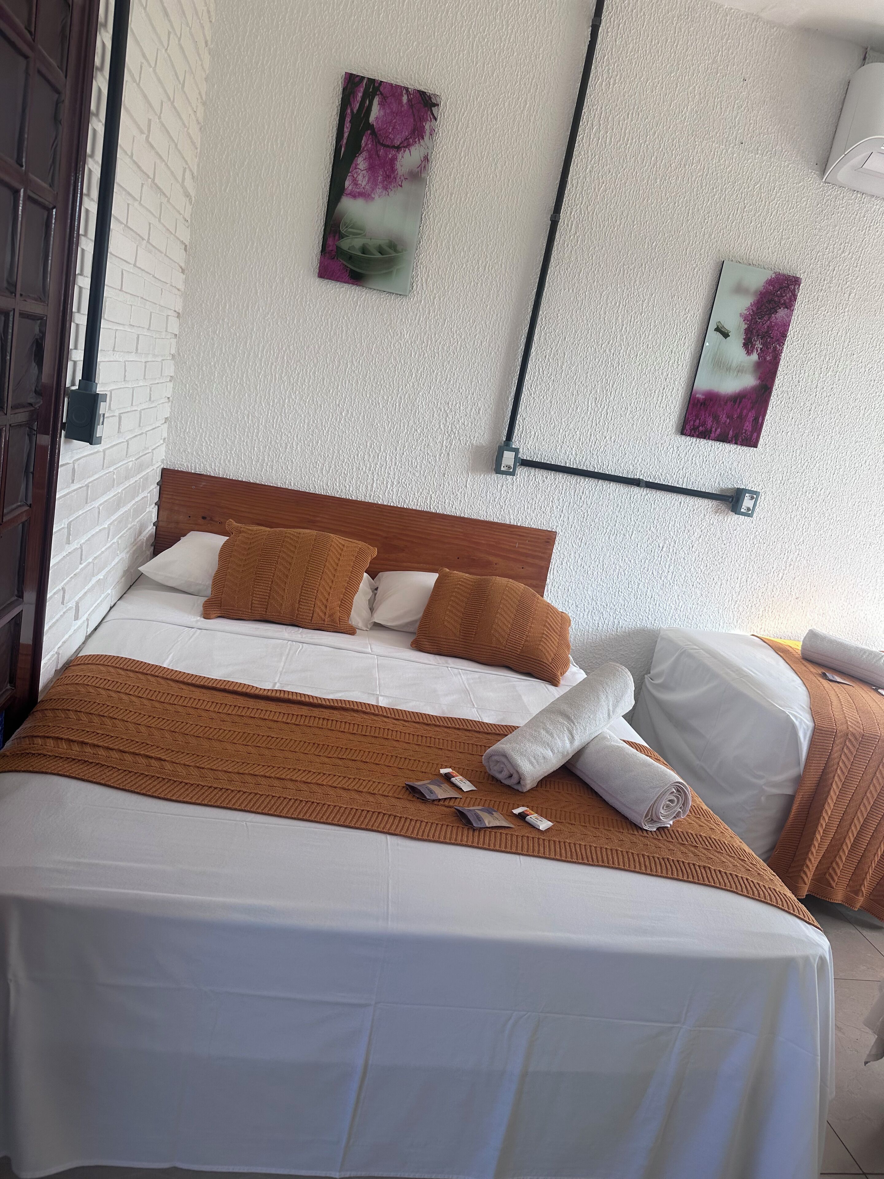 Un lit bien fait, avec une couverture et des oreillers marron, une tête de lit blanche et deux tableaux accrochés au mur.