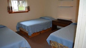 Ein Zimmer mit zwei Einzelbetten, einem kleinen Schreibtisch und einem Fenster mit Vorhängen.