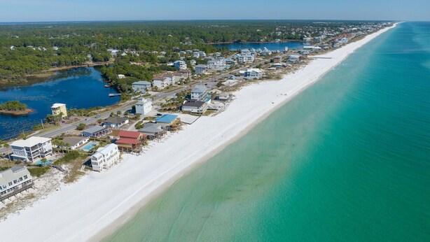 An aerial view of a coastal town with a long sandy beach, clear turquoise waters, and a mix of residential buildings. - Sunset Bungalow on 30A - AWESOME SPOT ON30A- 4BR/2BA, Fabulous Views of the Gulf (Santa Rosa Beach)