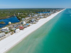 Eine Luftaufnahme einer Küstenlandschaft mit einem langen Sandstrand, klarem blauen Wasser und einer Mischung aus Wohngebäuden.