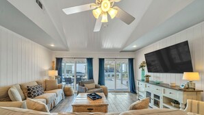 A spacious living room with a ceiling fan, a flat-screen TV, and a view through the glass doors to the outside. - Sunset Bungalow on 30A - AWESOME SPOT ON30A- 4BR/2BA, Fabulous Views of the Gulf (Santa Rosa Beach)