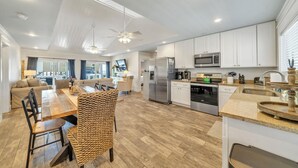 A spacious kitchen with white cabinets, stainless steel appliances, and a dining area with a wooden table and woven chairs. - Sunset Bungalow on 30A - AWESOME SPOT ON30A- 4BR/2BA, Fabulous Views of the Gulf (Santa Rosa Beach)