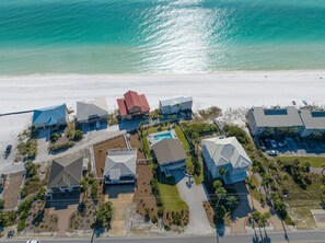 Vista aérea de uma área residencial costeira com casas, piscina e praia.