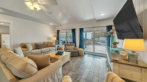 A spacious living room with a large sofa set, a coffee table, and a ceiling fan. There is a sliding glass door leading to an outdoor deck. - Sunset Bungalow on 30A - AWESOME SPOT ON30A- 4BR/2BA, Fabulous Views of the Gulf (Santa Rosa Beach)