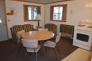 A compact living room with a round table, plaid furniture, a stove, and a window with curtains. - Family vacation on Black Lake with a private beach! (Hammond)