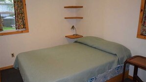 Un lit simple avec une couvre-lit verte, une table de chevet et une petite table de nuit avec une lampe.