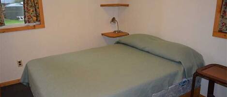 A single bed with a green bedspread, a bedside table, and a nightstand with a lamp.