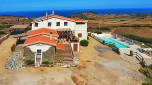 A two-story building with a red-tiled roof, a swimming pool, and a stone facade. - azienda agrituristica Finagliosu (Sassari)