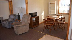 Ein Wohnzimmer mit Sofa, Sessel, Fernseher und Esstisch mit Stühlen.