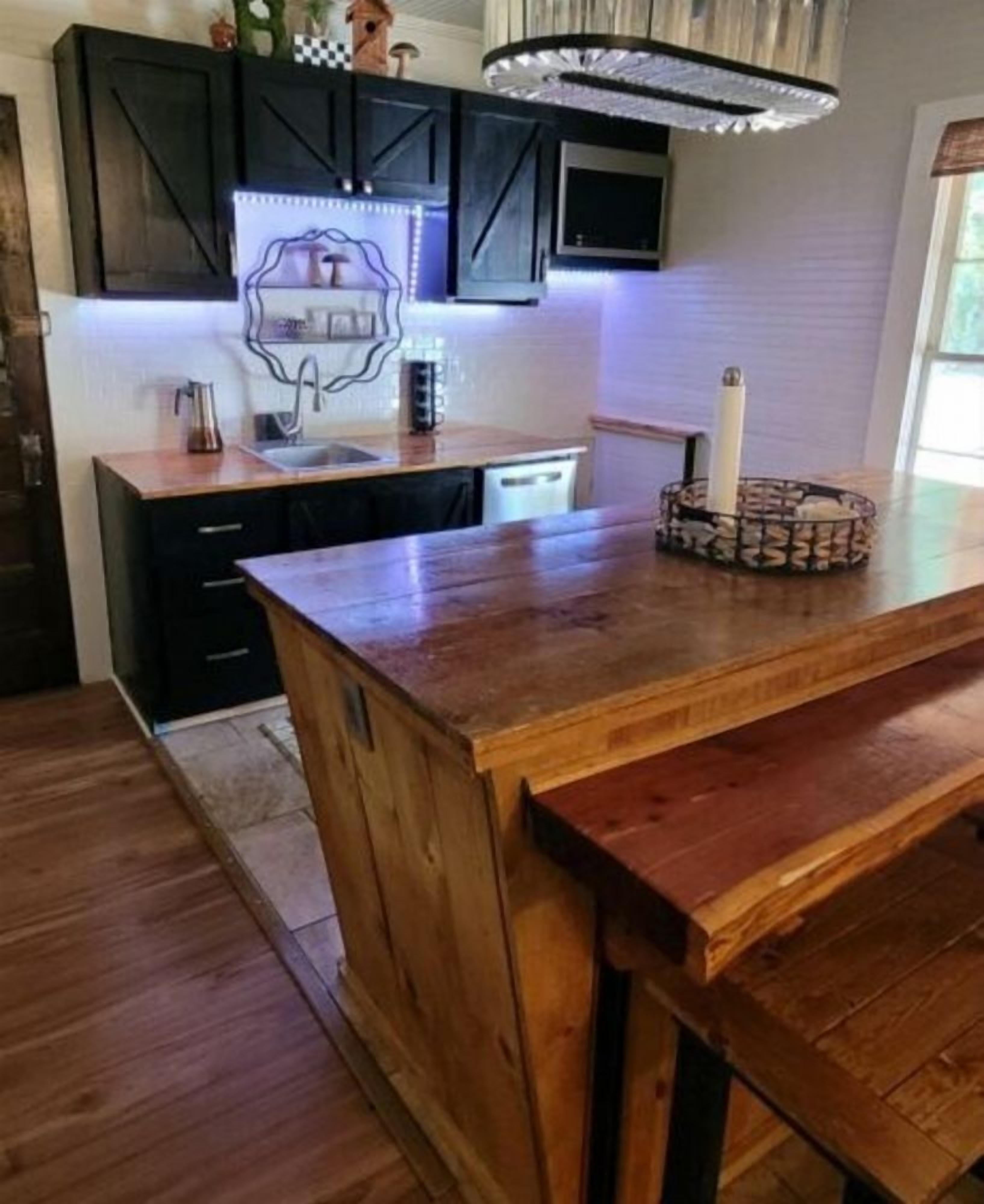 A kitchen with dark wooden cabinets, a wooden island, and a modern pendant light.