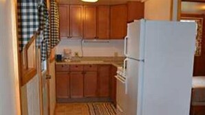 A compact kitchen with wooden cabinets, a white refrigerator, and a dining area with a table and chairs. - Family vacation on Black Lake with a private beach! (Hammond)