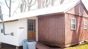 A small, single-story wooden structure with a gabled roof, a front door, and a side window. - Family vacation on Black Lake with a private beach! (Hammond)