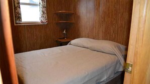 A small, wooden-paneled room with a single bed, a nightstand, and a window with floral curtains. - Family vacation on Black Lake with a private beach! (Hammond)