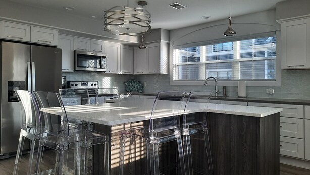 A modern kitchen with a central island, stainless steel appliances, and a large window providing natural light. - Spacious 3 Room Condo Near Michigan's Piers and Waterways (Grand Haven)